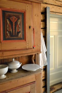 Noe av det gamle fine serviset får stå fremme. Ved siden av skapet henger mors egenvevde linhåndkle, med en A sirlig brodert i hjørnet. 